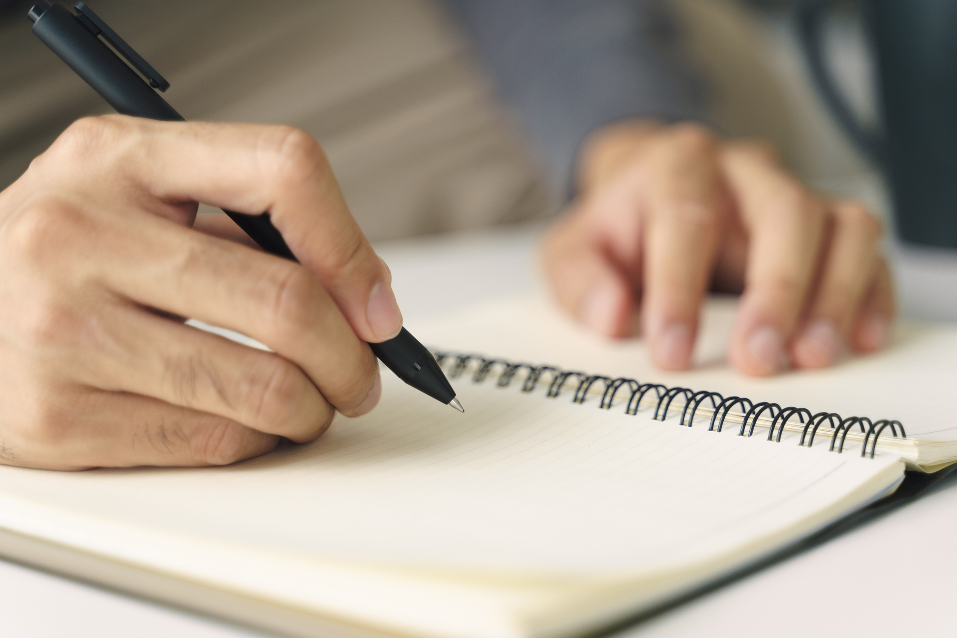 1920-close-up-of-young-man-in-casual-cloth-hands-writing-down-on-the-notepad-notebook-using-ballpoint-pen-on-the-table.jpg