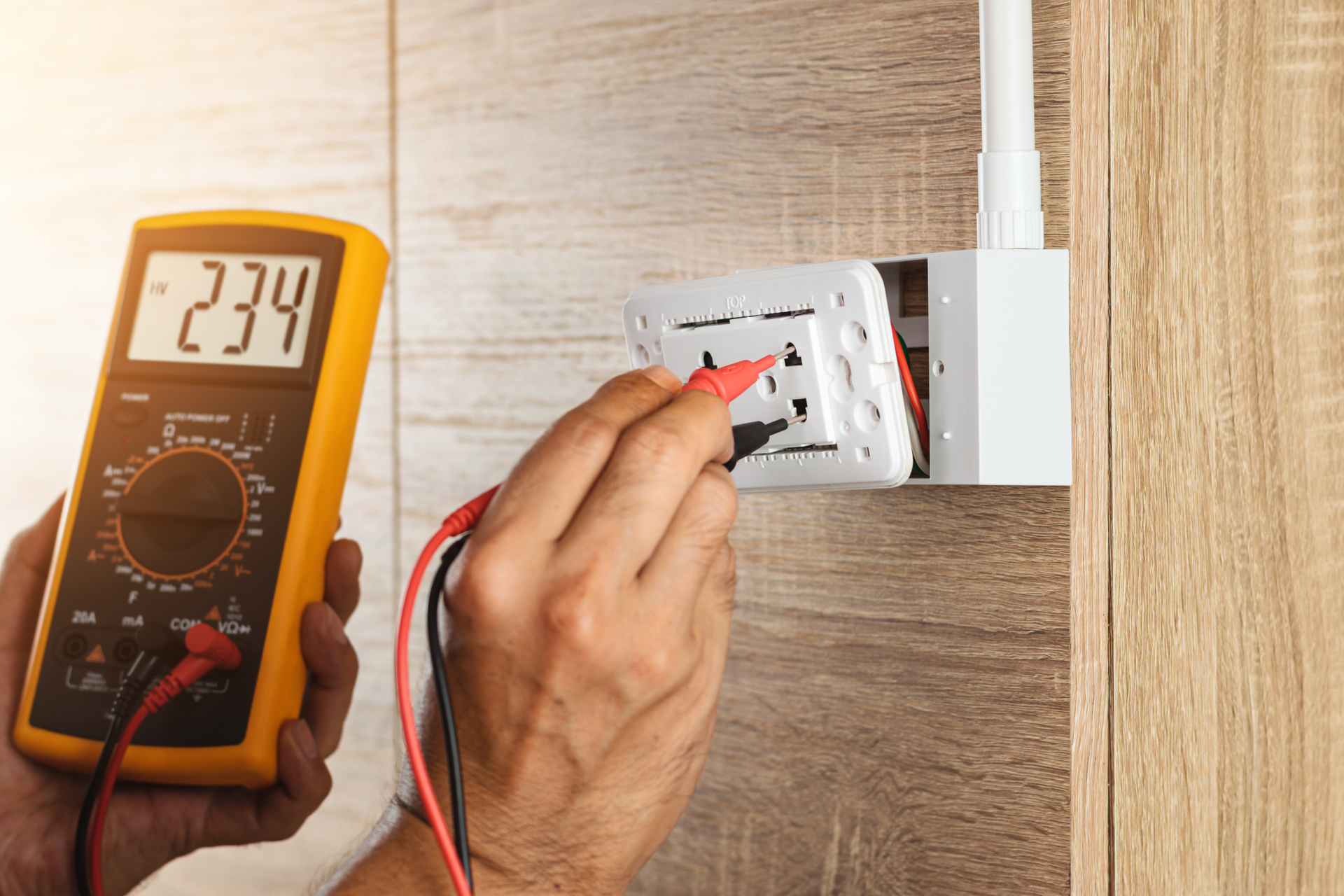 1920-electrician-using-a-digital-meter-to-measure-the-voltage-at-a-wall-socket-on-a-wooden-wall.jpg