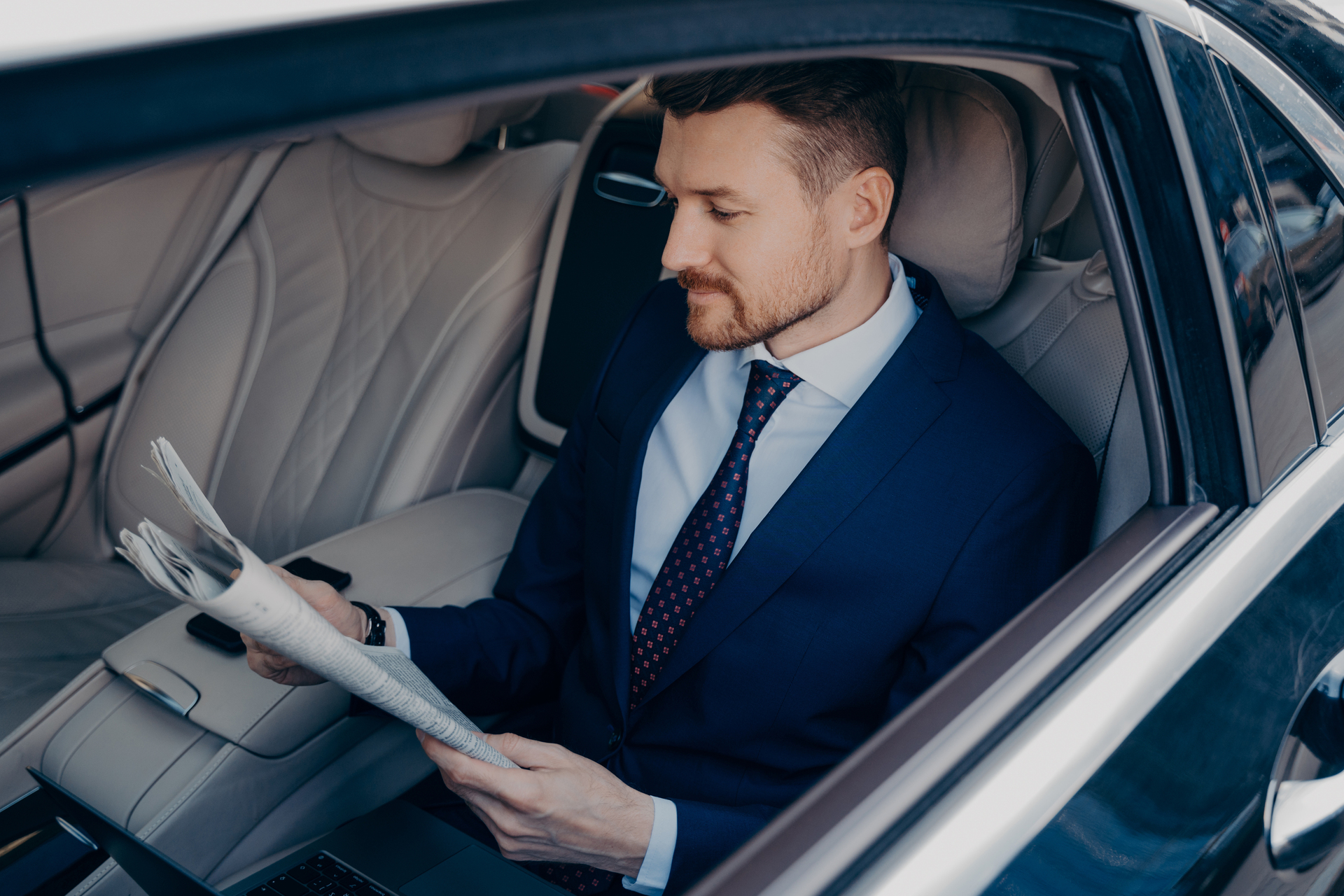 1920-thoughtful-executive-manager-in-formal-suit-reading-newspaper-in-backseat-of-limousine.JPG